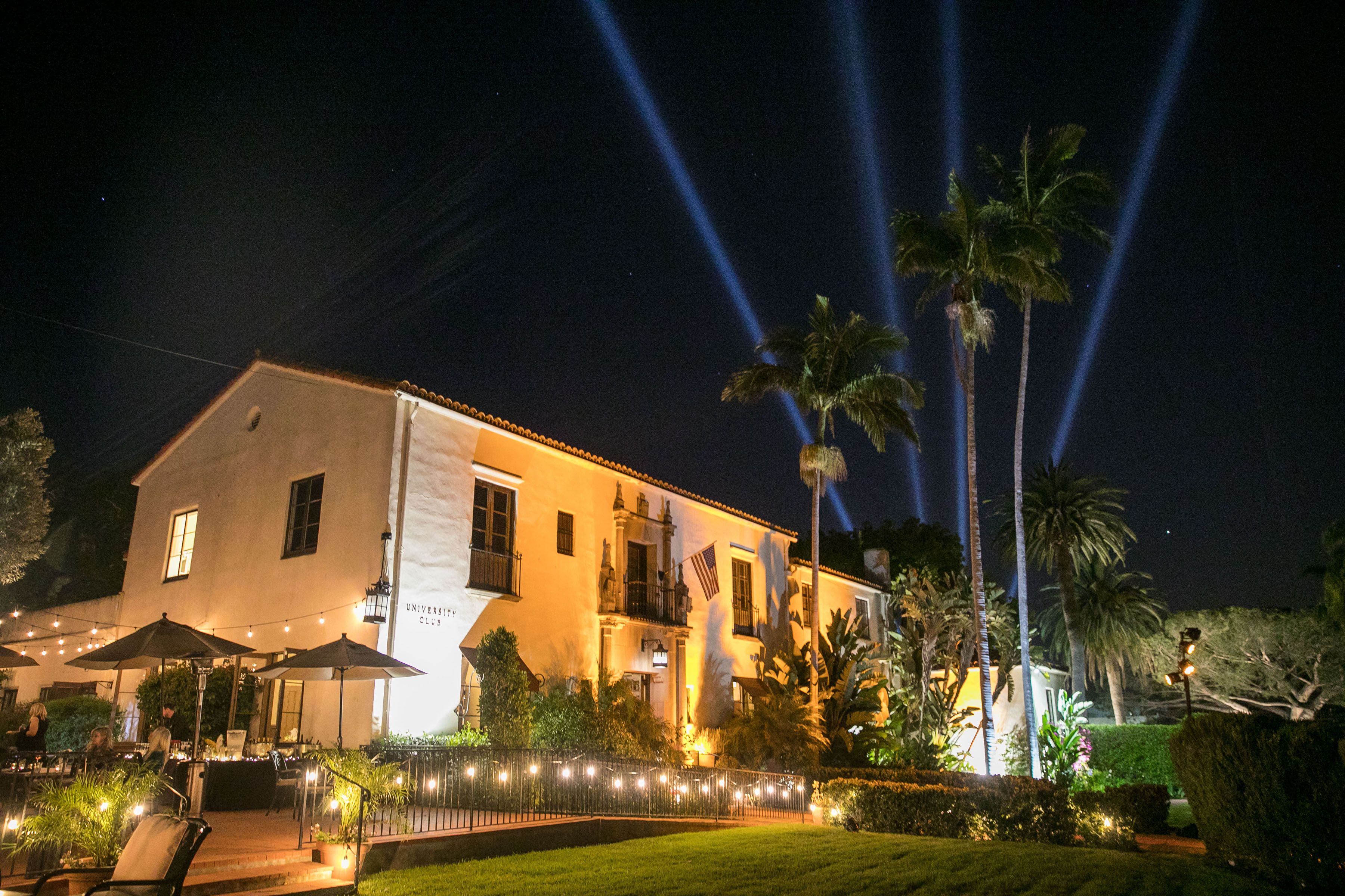 The exterior of the UCSB University Club, dramatically lighted at night and complemented by palm trees.